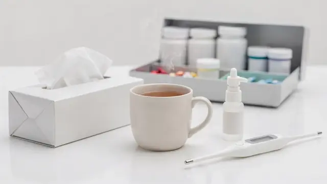 Erkältungsmittel auf einem Tisch mit Thermometer, Nasenspray, Hustenmittel und Taschentüchern