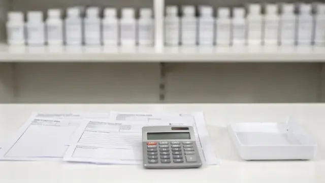 Apotheken-Theke mit Rezept, Taschenrechner und Arzneimittelschränken zum Thema Rezeptzuzahlung