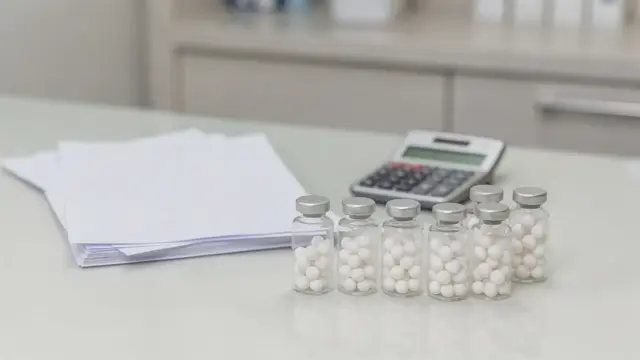 Homöopathie auf Kasse: Versicherungsunterlagen, Globuli und ein Arztpult in einer Praxis